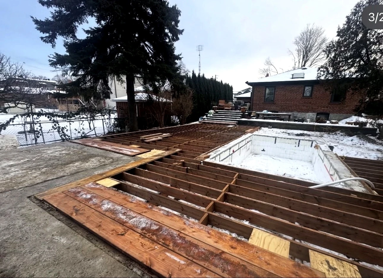 Real Pisces jobsite: wooden deck framing in snow beside a pool shell under construction