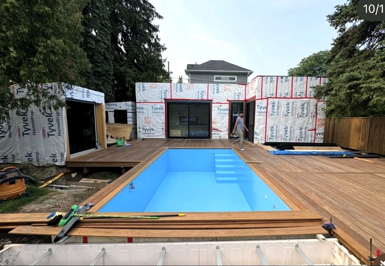 Real Pisces jobsite in summer: pool and deck front view with the weather-wrapped suite behind