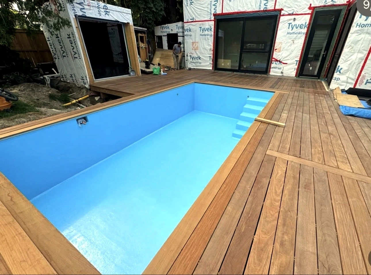 Real Pisces jobsite in summer: blue pool close-up with the finished wood deck